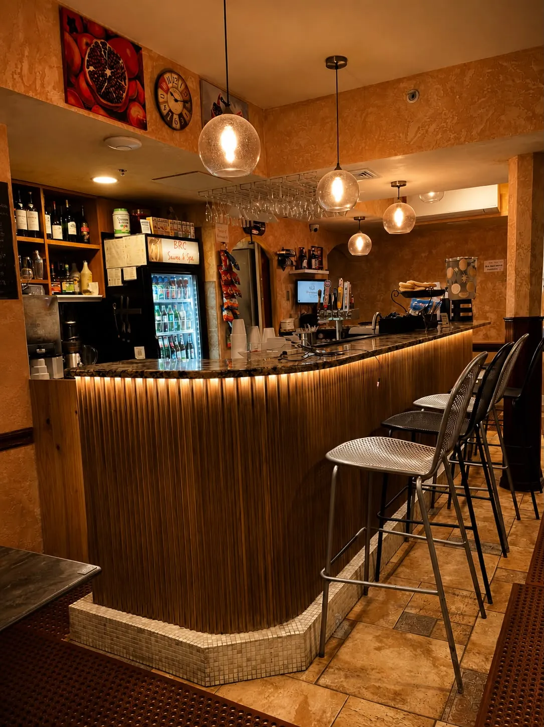 BRC's bar: a curved wooden counter lit from beneath, stools, pendant lamps and a drinks fridge.