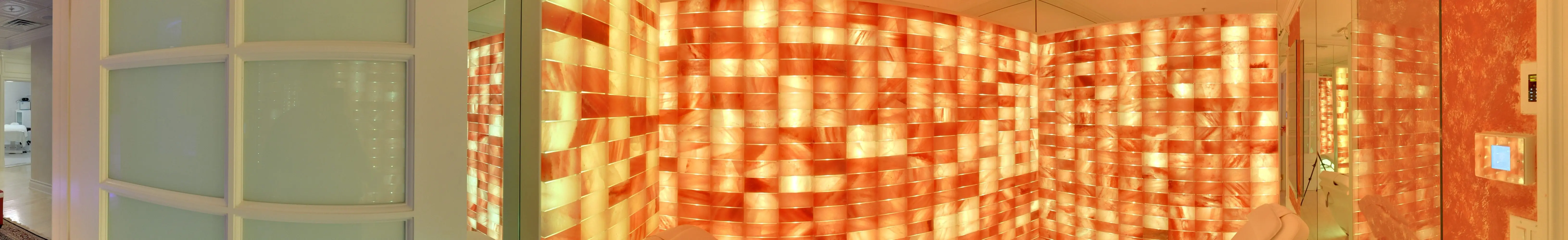 Walls of backlit Himalayan salt brick, glowing amber and rose, with a lounger in the corner.